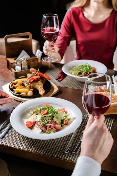 Genç çift restoranda bir kadeh kırmızı şarabı paylaşıyor, kutlama yapıyor ya da romantik bir buluşmada. Aşıklar restoranda şarap içer.