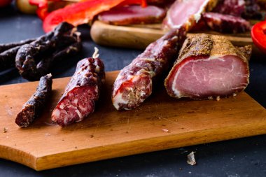 Tütsülenmiş ve kurutulmuş et, kurutulmuş jambon, tuzlanmış biltong eti, füme peynir, ahşap tepside taze sebzeler. Tatilin ürünleri. Metnin için boş yer.