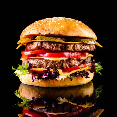 Ev yapımı, duble peynirli burger. Köfteli leziz bir burger, siyah masada, yakın plan. Metin için boşluk
