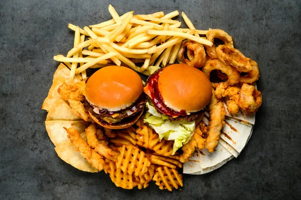 Combo large set of fast food burgers french fries and snacks. Juicy delicious hamburger, French fries, chicken legs and sauce. Served on black background. Fast food restaurant. Food delivery.