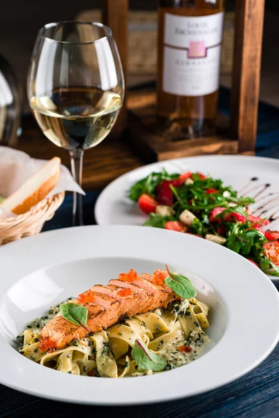 Somon ve krema soslu makarna. Somon ve havyarlı makarna bir bardak beyaz şarapla birlikte beyaz bir tabakta.
