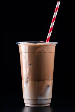 Plastik bardakta buzlu soğuk kakao, plastik bardakta siyah arka planda saman izole edilmiş buzlu çikolata içeceği.