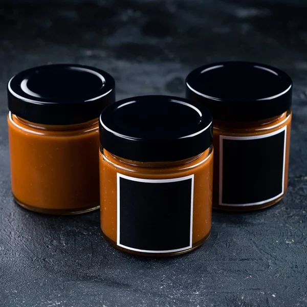 Homemade salted caramel sauce in a vintage jar on a dark slate, stone or concrete background.