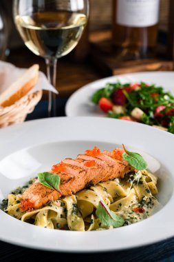 Somon ve krema soslu makarna. Somon ve havyarlı makarna bir bardak beyaz şarapla birlikte beyaz bir tabakta.