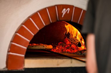 Pizza, odun yakan bir fırında kızartılır, açık ahşap fırında kürekle taze İtalyan pizzası pişirilir. Ateşli geleneksel tuğla ocak fırını. Pizzacı..