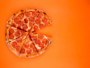 Turuncu arka planda pepperoni pizza, parlak bir portakalda pişti ve dilimlendi.