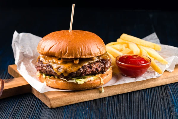 Close up of gourmet pub hamburger with bacon on wooden table, large burger with potatoes and ketchup close-up, big burger and some french fries