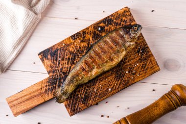 Kızarmış alabalık, ızgara alabalık ahşap bir tahtada sebzelerle servis edilir.