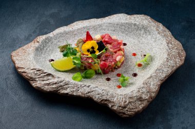 Koyu taştan bir arka planda ton balıklı taş tepsi.