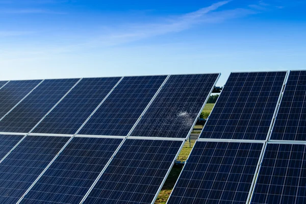 Painel solar quebrado entre painéis inteiros contra um céu azul — Fotografia de Stock