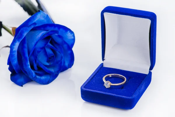 Golden engagement ring in a blue velvet box and blue rose (shallow DOF) — Stock Photo, Image