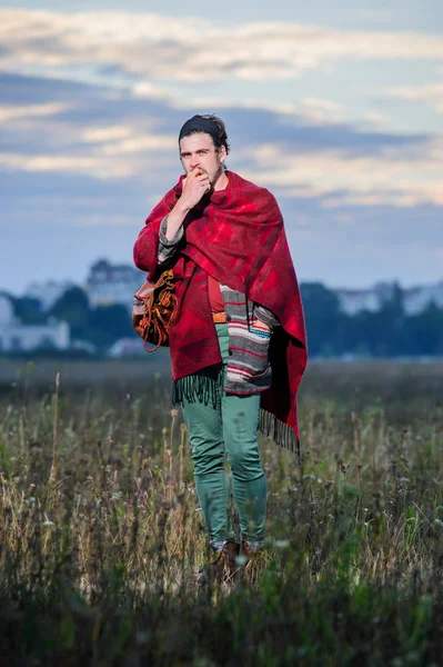 Giovane hippie uomo in poncho sul campo verde — Foto Stock