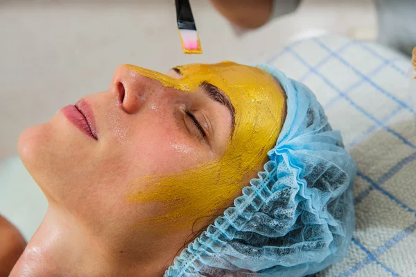 Mooie vrouw met gouden gezichtsmasker op beauty salon. — Stockfoto
