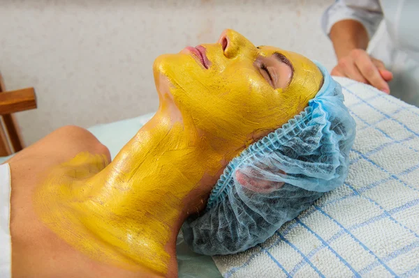 Όμορφη γυναίκα με χρυσή μάσκα προσώπου στο σαλόνι ομορφιάς. — Φωτογραφία Αρχείου
