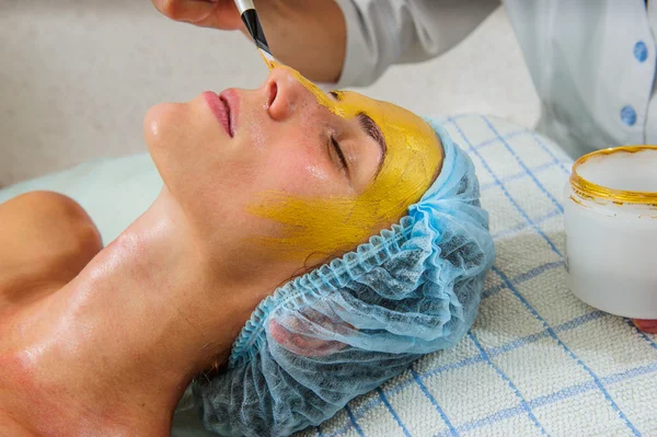 Hermosa mujer con máscara facial dorada en el salón de belleza . — Foto de Stock