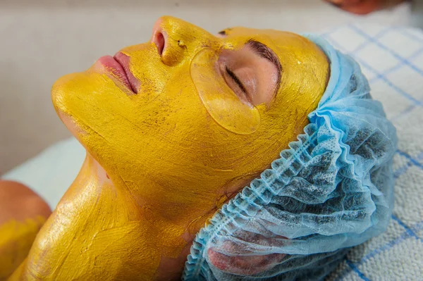 Hermosa mujer con máscara facial dorada en el salón de belleza . — Foto de Stock