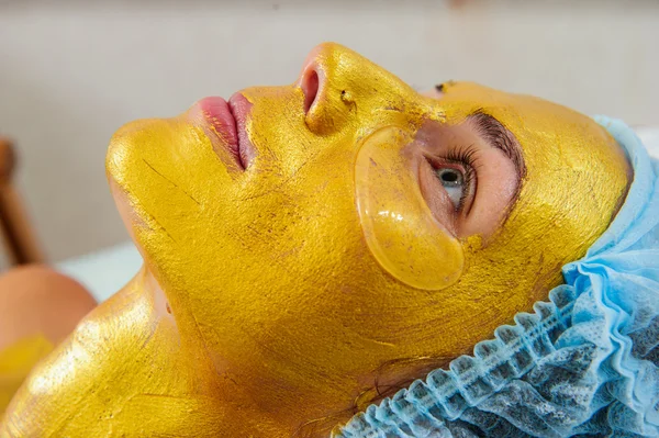 Schöne Frau mit goldener Gesichtsmaske im Schönheitssalon. — Stockfoto