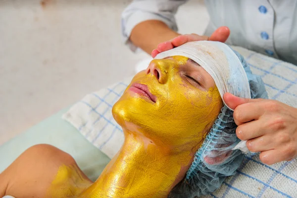 Hermosa mujer con máscara facial dorada en el salón de belleza . — Foto de Stock