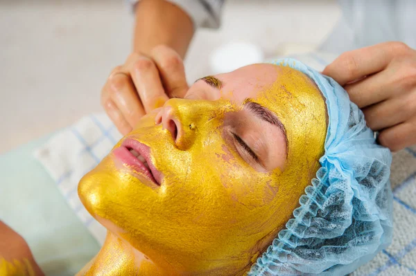 Schöne Frau mit goldener Gesichtsmaske im Schönheitssalon. — Stockfoto