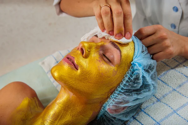 Belle femme avec masque facial doré au salon de beauté . — Photo