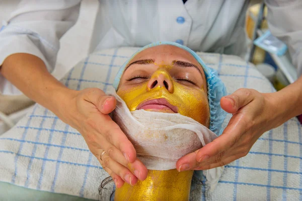 Belle femme avec masque facial doré au salon de beauté . — Photo