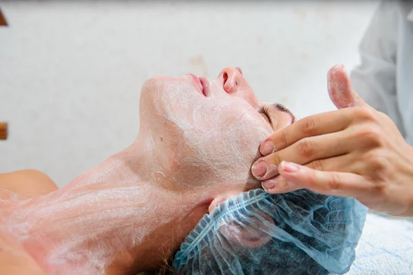 Mujer joven y relajada recibiendo un masaje facial con crema . — Foto de Stock