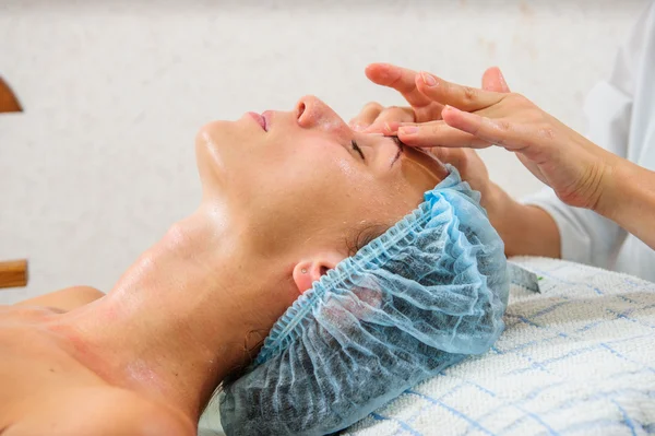 Mujer joven y relajada recibiendo un masaje facial . — Foto de Stock