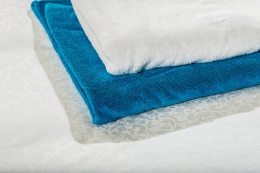 White and blue clean towels stacked on the  bed .