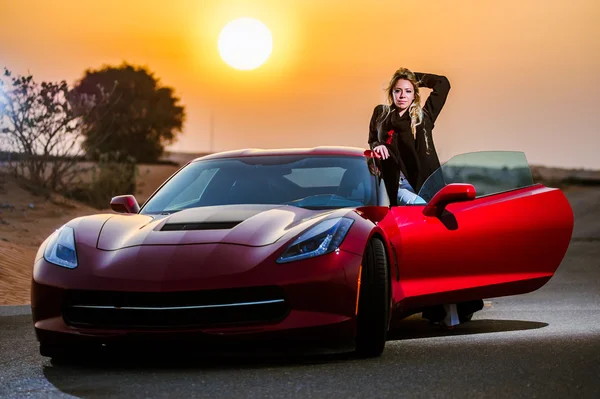 Arabic way dressed yang woman posing in red car in desert. — Stock Photo, Image