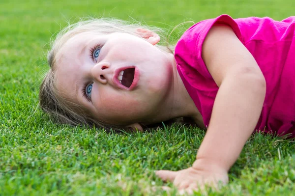Klein schattig Europees meisje poseren in het groene gras. — Stockfoto