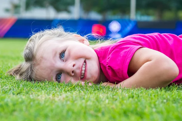 Small cute European girl posing lying down in the green grass. — Stock Photo, Image