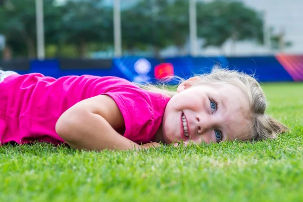 Small cute European girl posing lying down in the green grass. — Stock Photo, Image