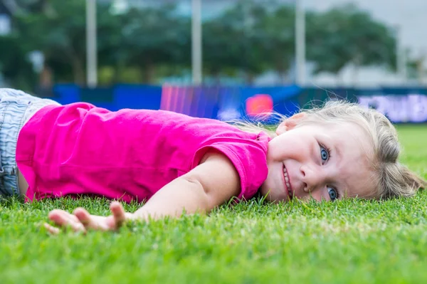 Small cute European girl posing lying down in the green grass. — Stock Photo, Image