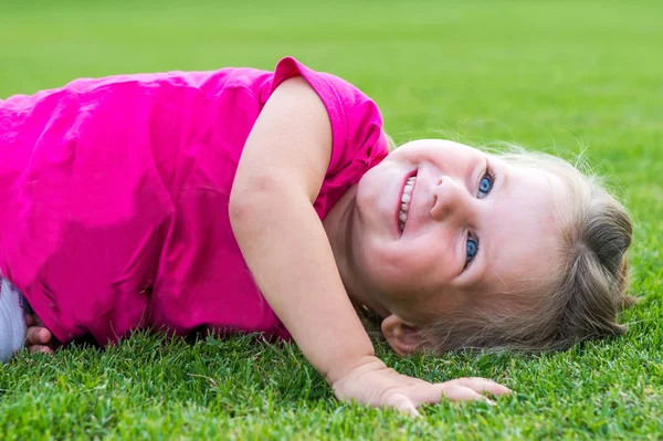 Kleines süßes europäisches Mädchen posiert liegend im grünen Gras. — Stockfoto