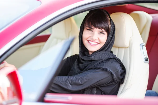 Maneira árabe vestido yang mulher posando em carro vermelho no deserto . — Fotografia de Stock