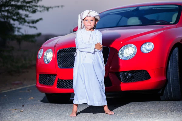 Pequeno menino árabe posa na frente do carro vermelho . — Fotografia de Stock