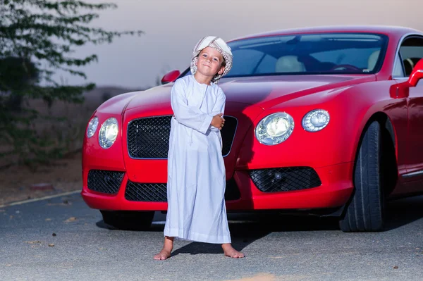 Pequeno menino árabe posa na frente do carro vermelho . — Fotografia de Stock