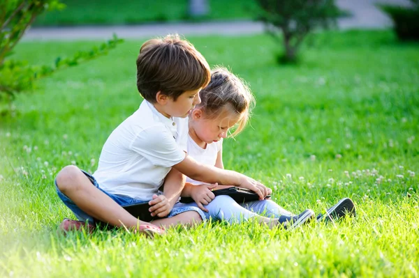 Dos niños europeos usando la tableta táctil PC en la hierba Imagen De Stock