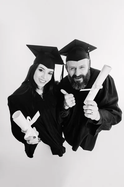 Two happy graduating adult students isolated on grey background black and white — Stock Photo, Image