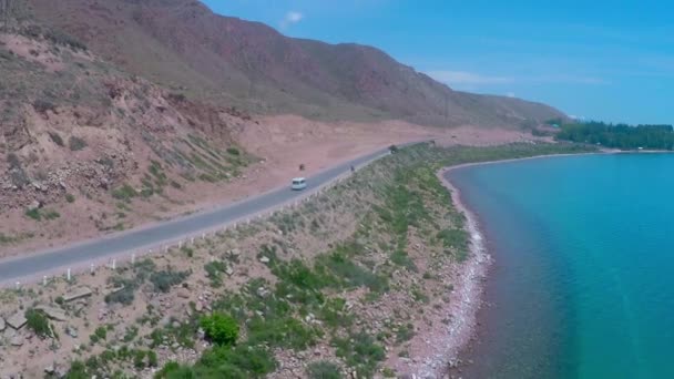 Antenn video av små vita bussar går på vägen längs bergiga havsstranden — Stockvideo