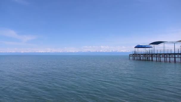 Muelle vacío, lago y lejanos picos de nieve en el horizonte. 4K día soleado pan tiro — Vídeo de stock