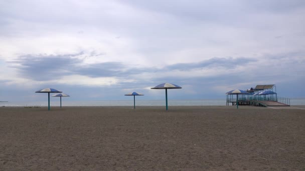 Порожній піщаний пляж і великі сонячні парасольки в похмурий день. Відео з низьким сезоном 4K — стокове відео