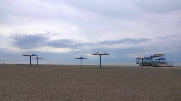 Playa de arena vacía y grandes sombrillas en un día nublado. 4K tiro panorámico de temporada baja — Vídeos de Stock