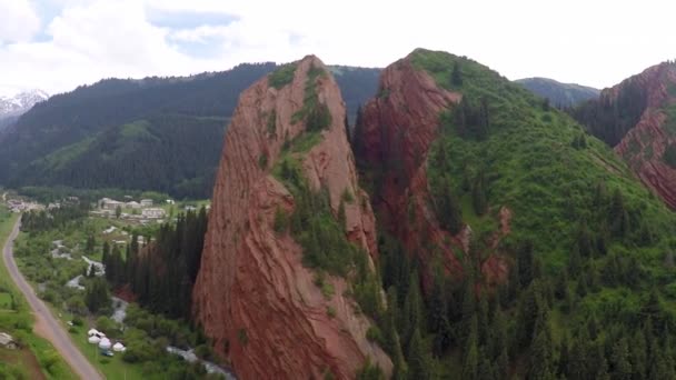 Gestreepte oranje rotsen, groene heuvels, besneeuwde toppen en vallei dorp luchtfoto video — Stockvideo