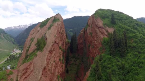 Gestreepte oranje rotsen, groene heuvels, besneeuwde toppen en vallei dorp luchtfoto video — Stockvideo