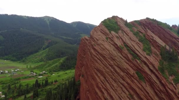 Rocas naranjas rayadas, colinas verdes, picos nevados y vídeo aéreo del pueblo del valle — Vídeos de Stock