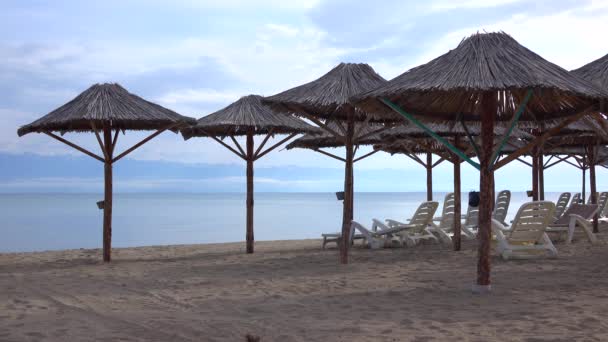 Empty beach, cane sun umbrellas and sunbeds against distant snow peaks. 4K video — Stock Video