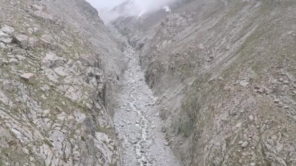 Воздушная камера, следующая за горным потоком на дне серого горного каньона — стоковое видео