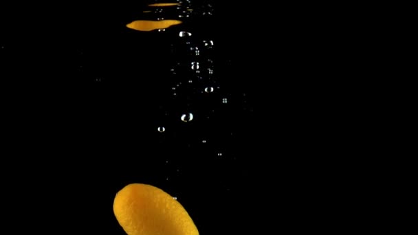 Ένα πορτοκαλί κουμκουάτ πέφτει κάτω από το νερό με εξαιρετικά αργή κίνηση. Μαύρο φόντο — Αρχείο Βίντεο