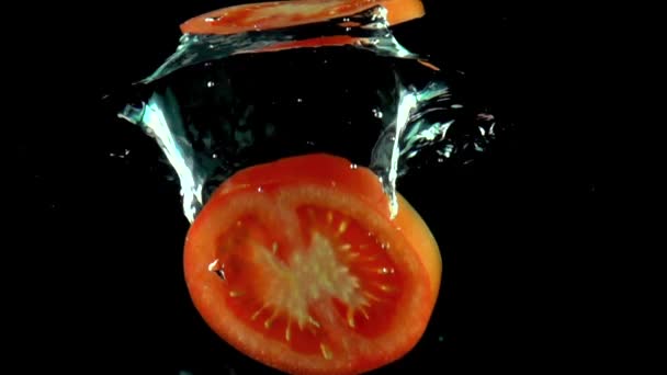 물 아래 떨어지는 빨간 토마토 슬라이스 슈퍼 슬로우 모션 샷. 검은 색 배경 — 비디오
